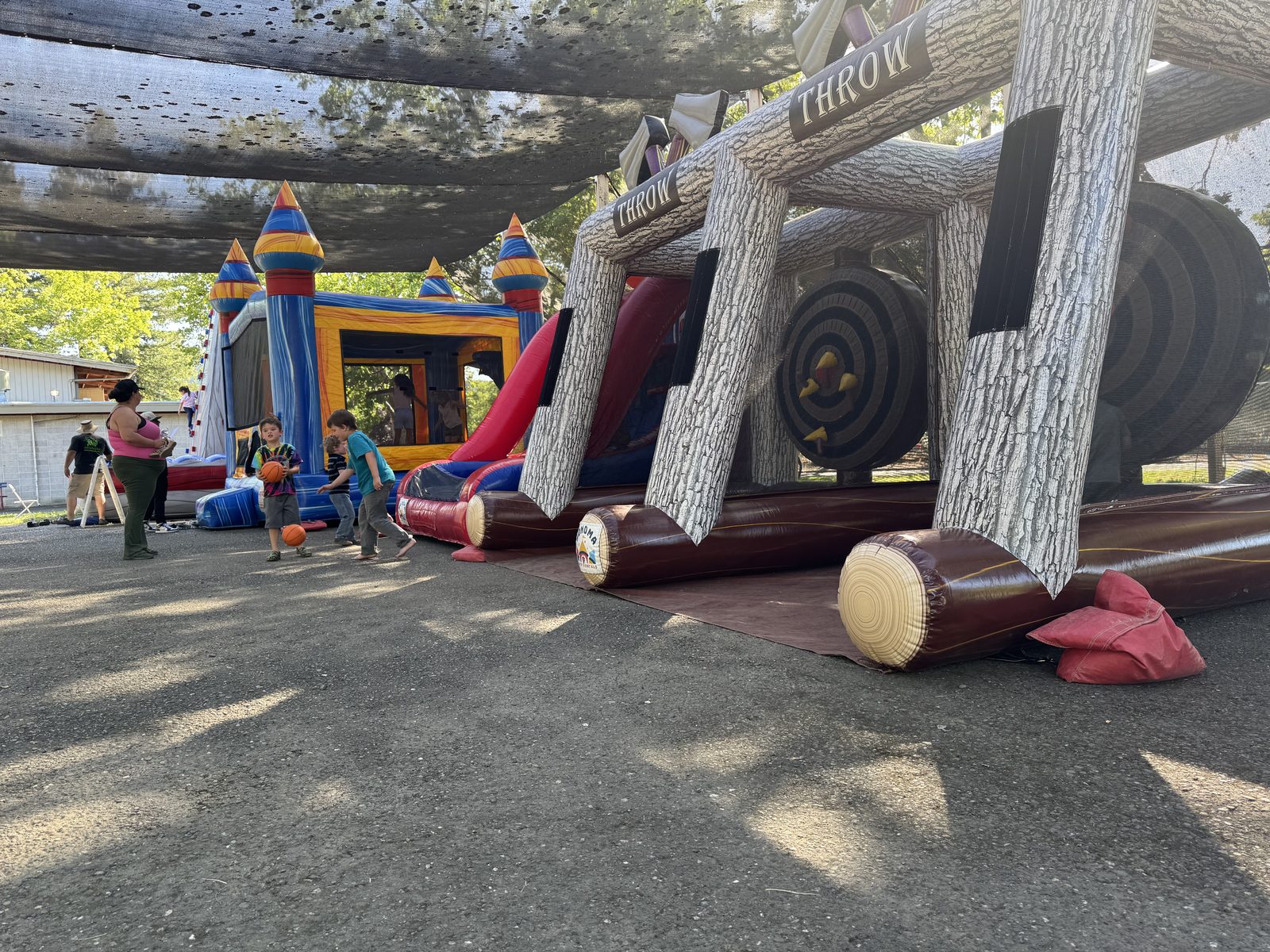An inflatable axe throw game and a castle bounce house combo set up under shade cloth at an event at the Calistoga Fairgrounds, with kids playing nearby